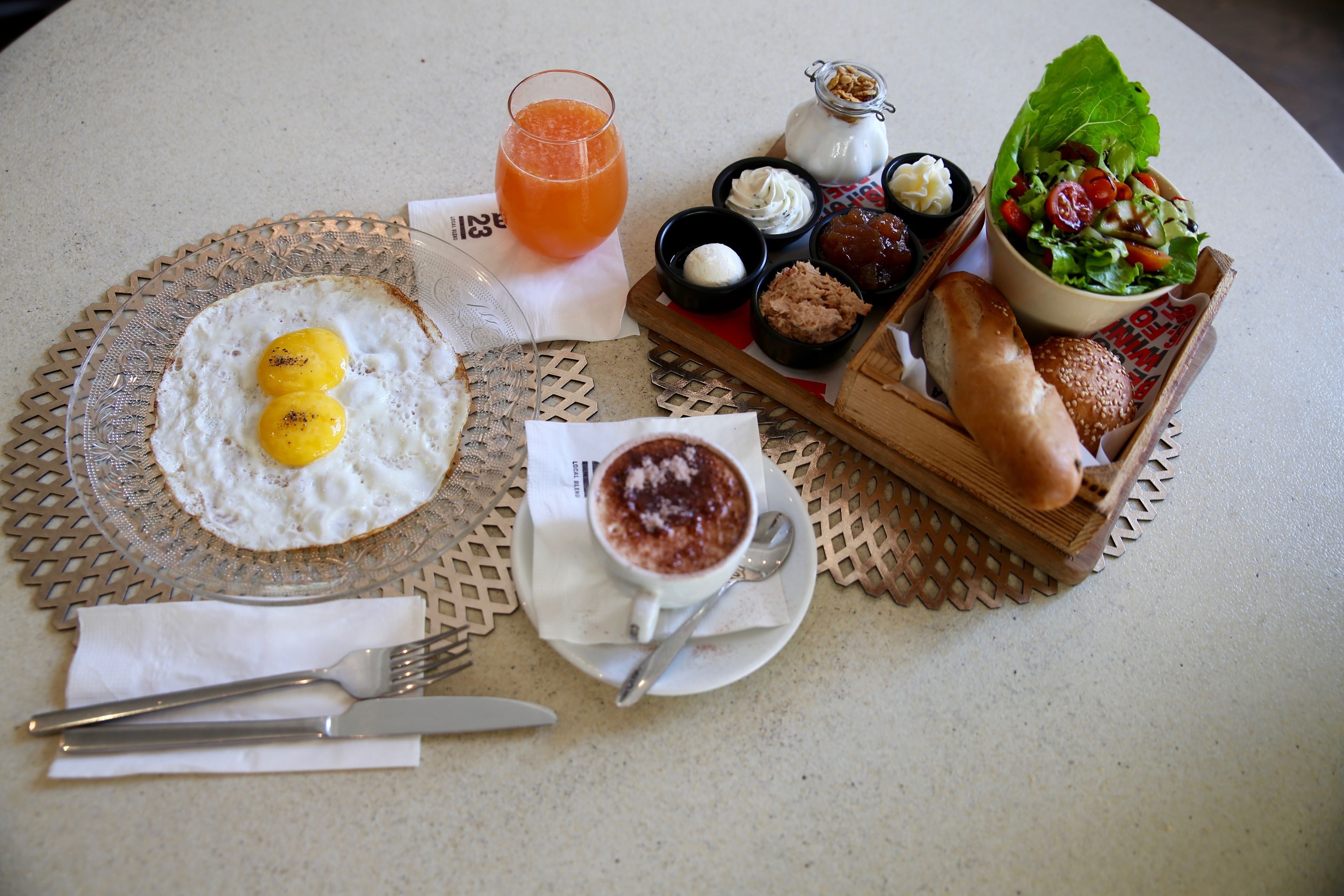 Un desayuno con huevos, tostadas, un vaso de zumo de naranja, ensalada en un bol y una taza de café.