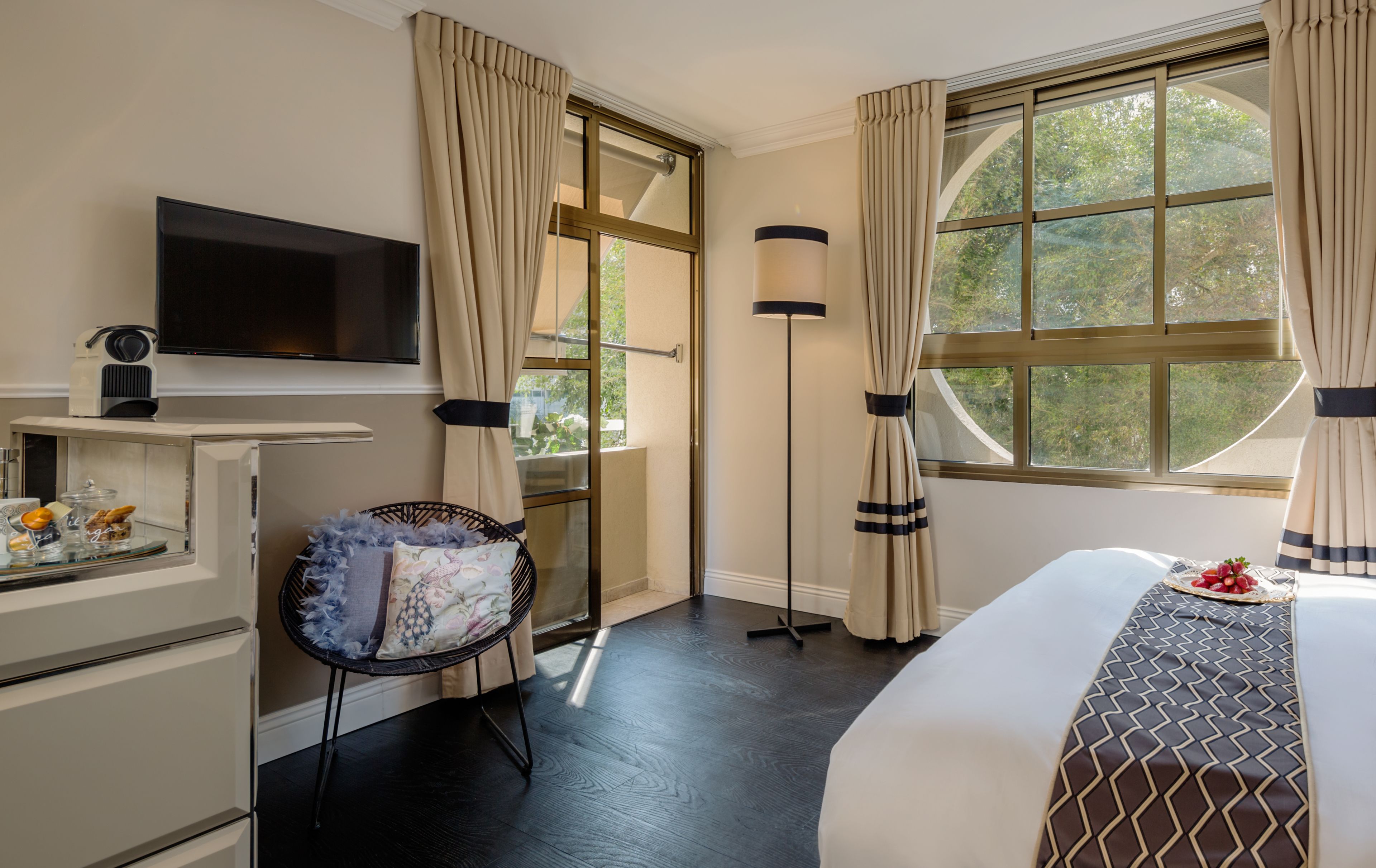 A hotel room with a bed, a desk with a television, a chair, a floor lamp, and a window with curtains.