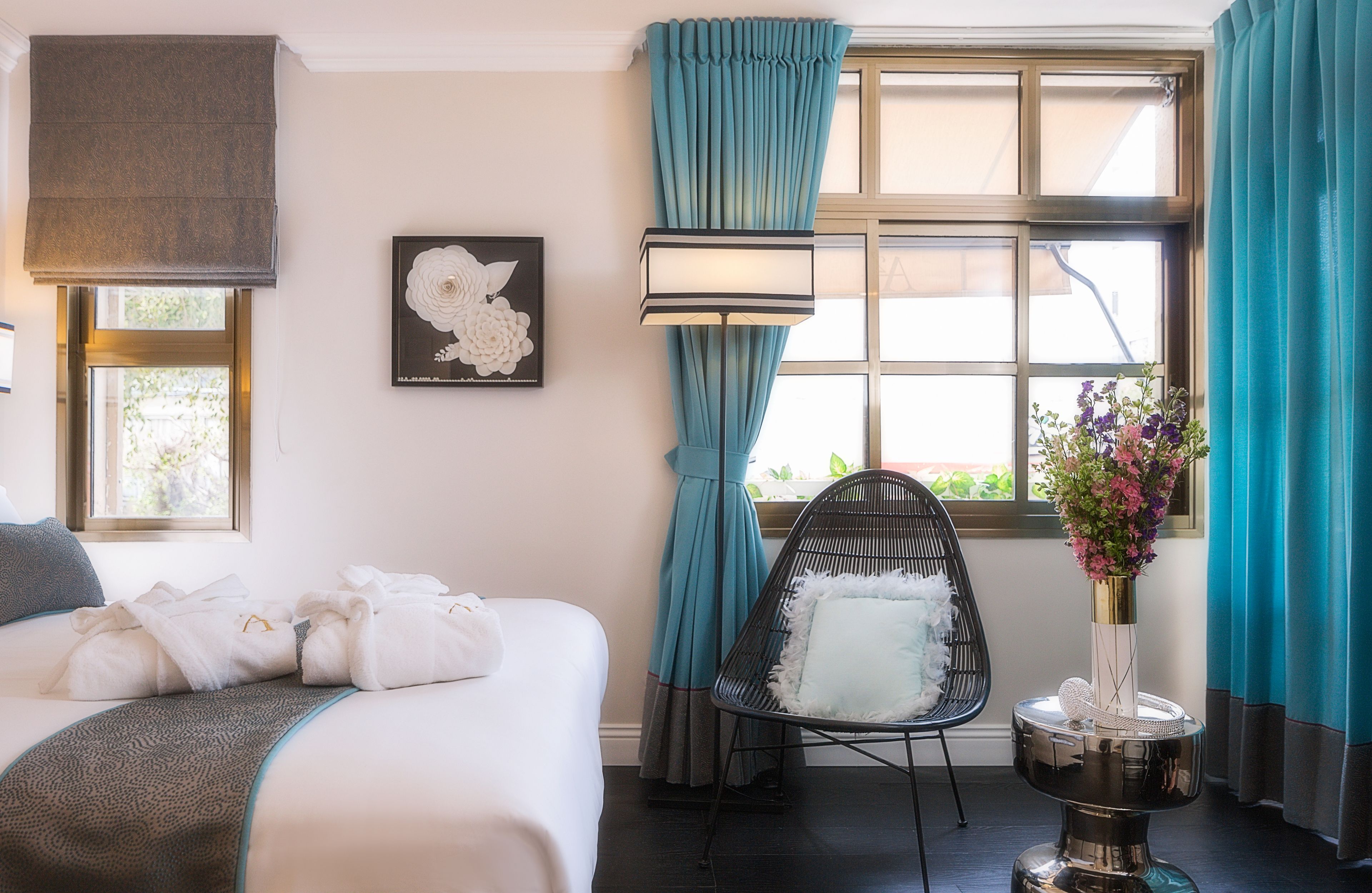A hotel room with a bed, a chair, a vase with flowers, and a window with curtains.