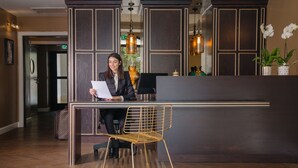 A reception desk with a woman reading a paper, a gold chair, and decorative vases. - A23 Boutique Hotel (Tel Aviv)