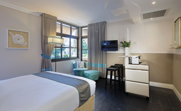 Une chambre d’hôtel avec un lit, un bureau, une chaise, une télévision et une fenêtre avec des rideaux.