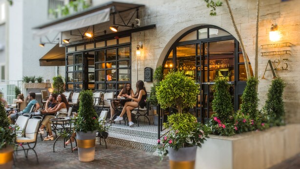 An outdoor seating area with tables and chairs, potted plants, and a building with a sign reading "A23". - A23 Boutique Hotel (Tel Aviv)