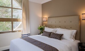 Un lit bien fait, recouvert d’une couvre-lit à motifs, un vase rempli de fleurs et une fenêtre avec des rideaux.