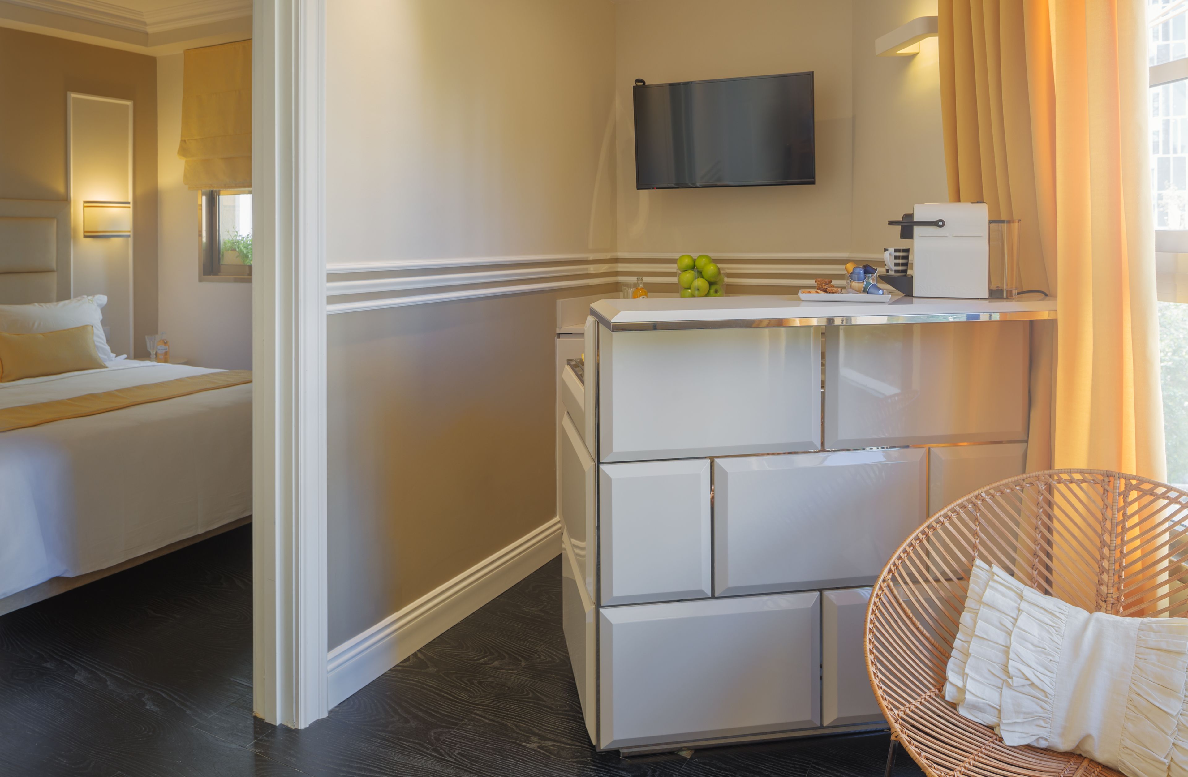 Una habitación de hotel con una cama, un minibar blanco, un televisor y una silla de mimbre.