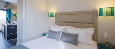 Een net opgemaakt bed met hoofdbord, twee nachtkastjes en een nachttafel met lamp.