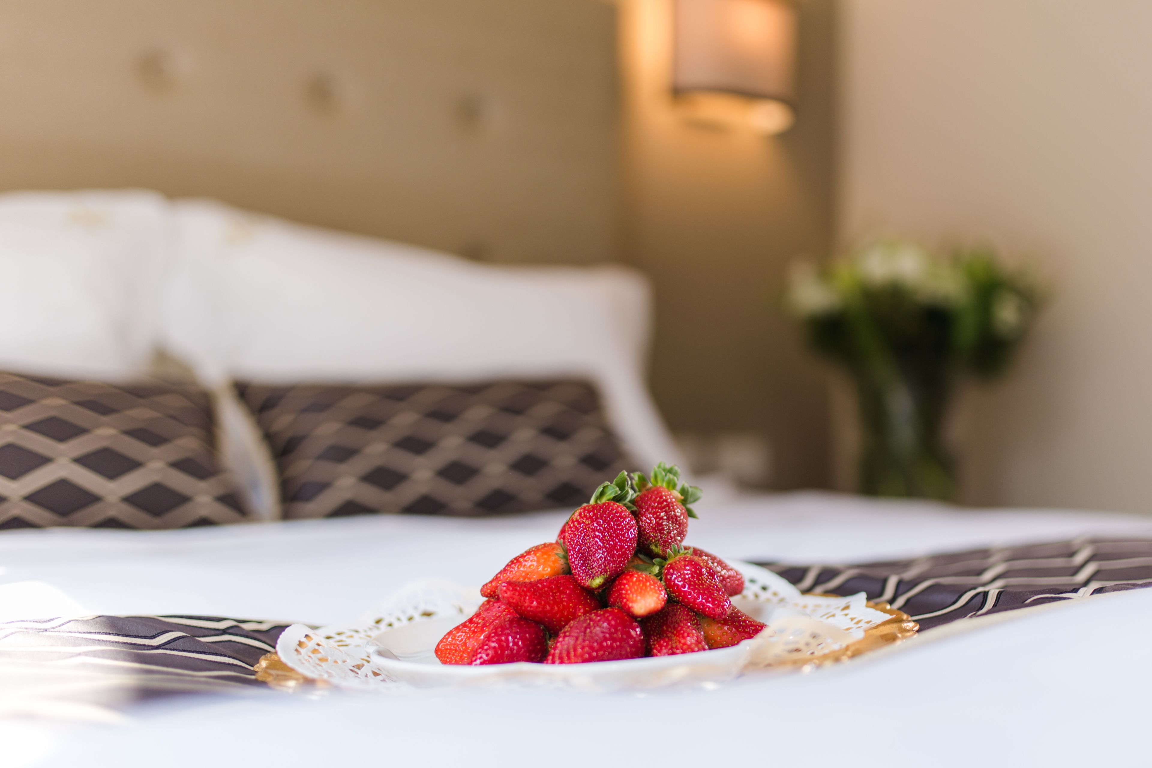 Una cama con un plato de fresas ordenado sobre un mantel individual blanco.