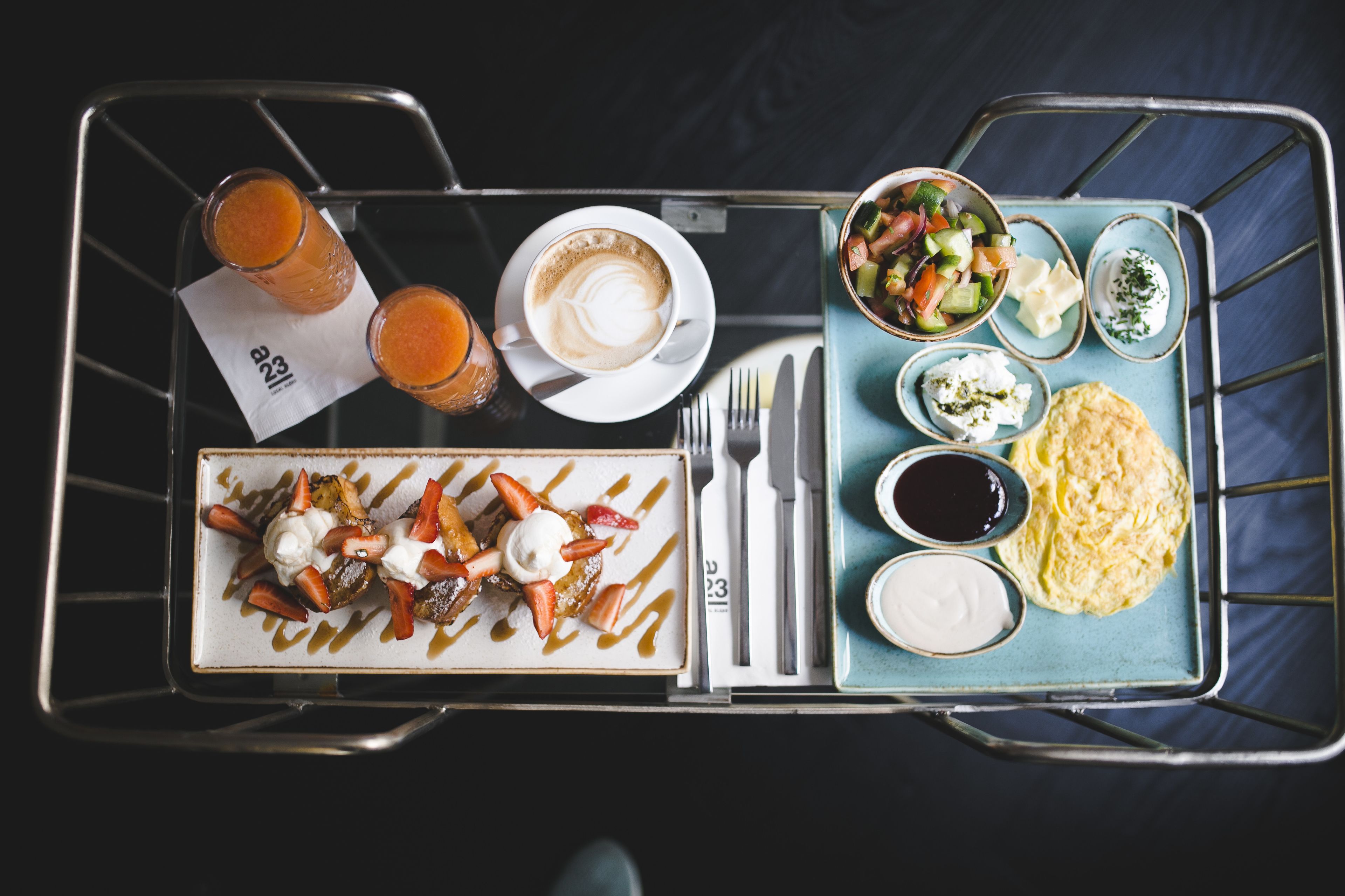Bandeja de comida con un plato de alimentos, dos vasos de jugo de naranja, una taza de café y un tazón de ensalada.