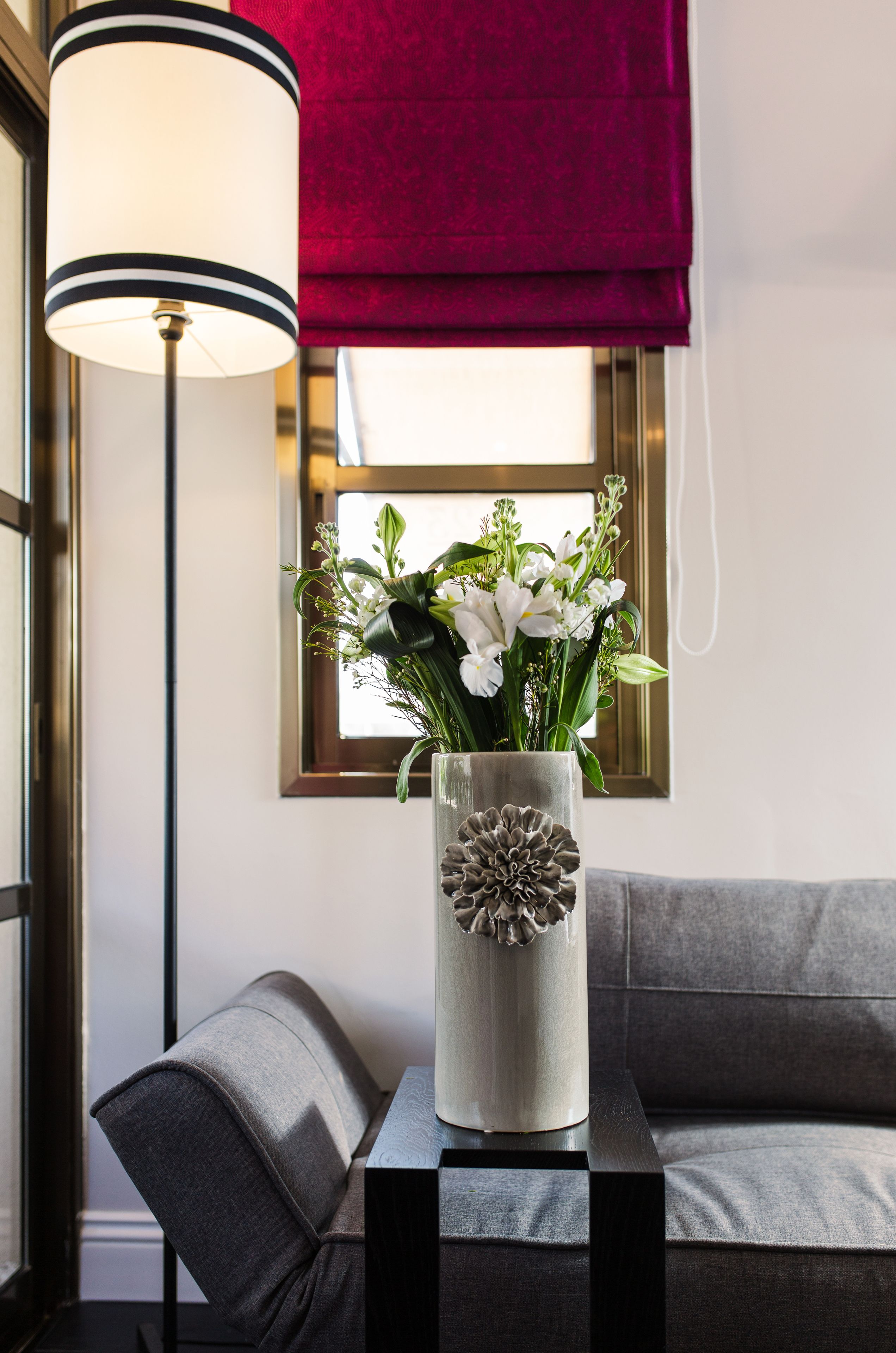 A modern living room with a grey sofa, a small black table, and a decorative vase with flowers.