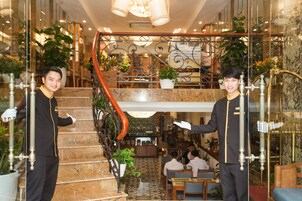 Un vestíbulo de hotel con una escalera de mármol, un comedor y una recepción.
