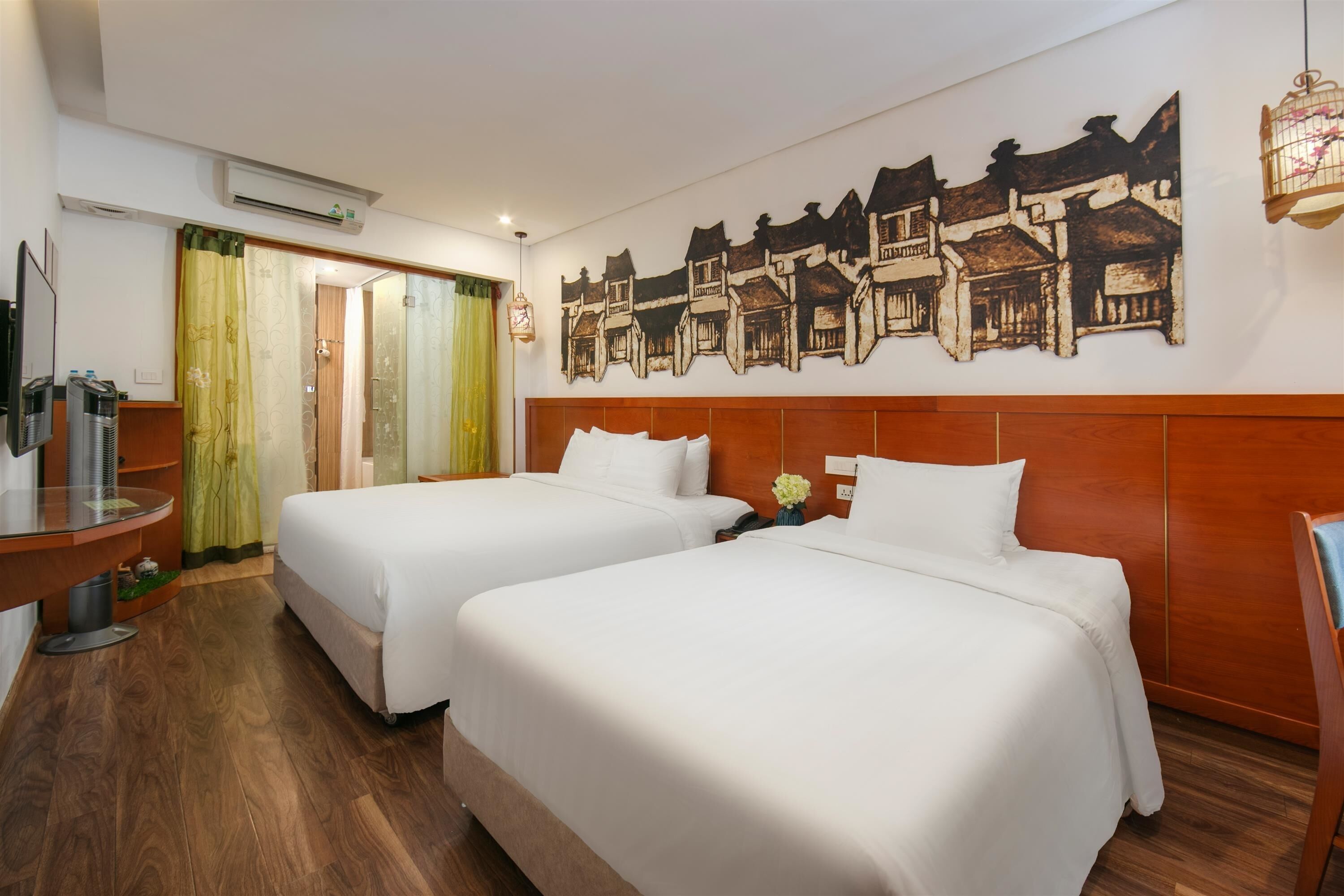 Une chambre d’hôtel avec deux lits, une tête de lit en bois, une fresque murale, une petite table et un téléviseur.