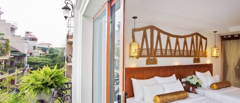 Habitación de hotel con una cama grande, dos mesitas de noche, un cabecero de madera y un balcón con plantas.