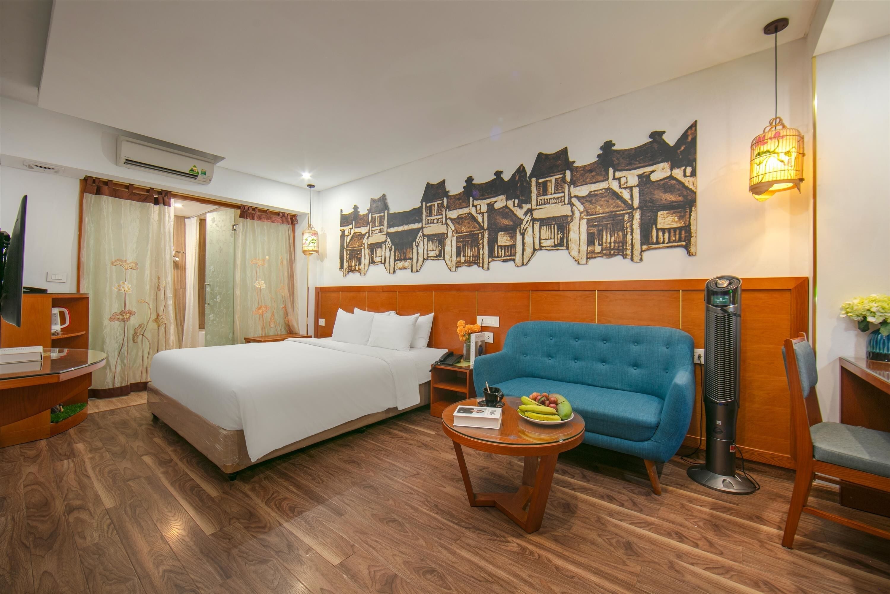 Een hotelkamer met een bed, een blauwe bank, een klein tafeltje met fruit, een elektrische kachel en een muurschildering.