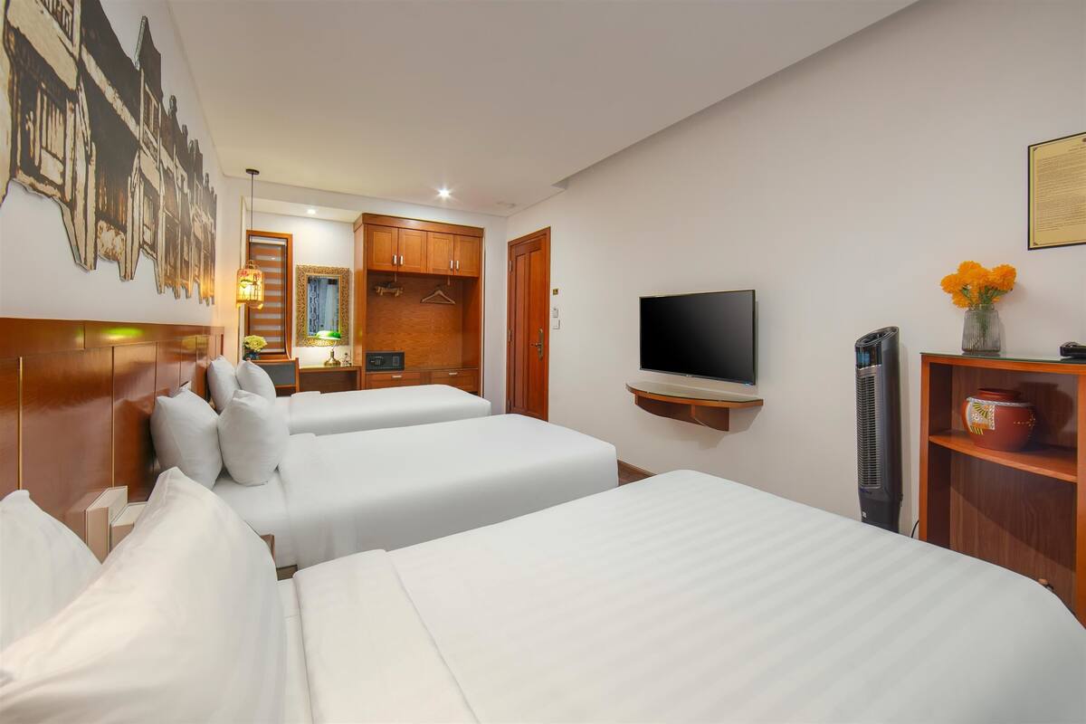 A hotel room with two beds, a television, a wardrobe, and a wall-mounted shelf with decorative items.