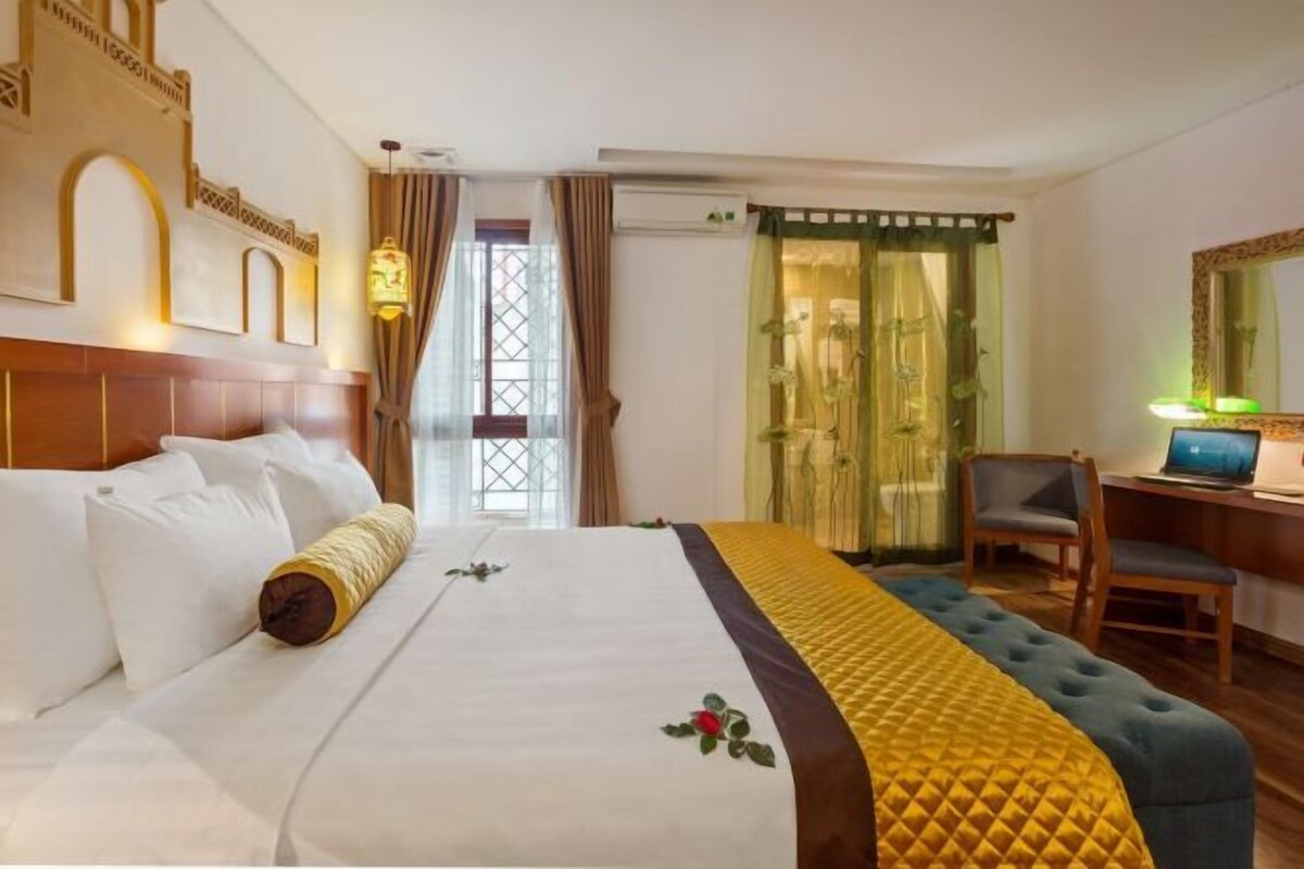 A hotel room with a large bed, a desk with a laptop, and a shower area.