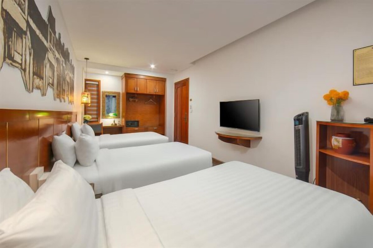 A hotel room with two beds, a television, a wardrobe, and a small table with a lamp.