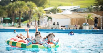Dos personas flotando sobre un flotador en una piscina, con vista clara de los alrededores, incluyendo un edificio y árboles.