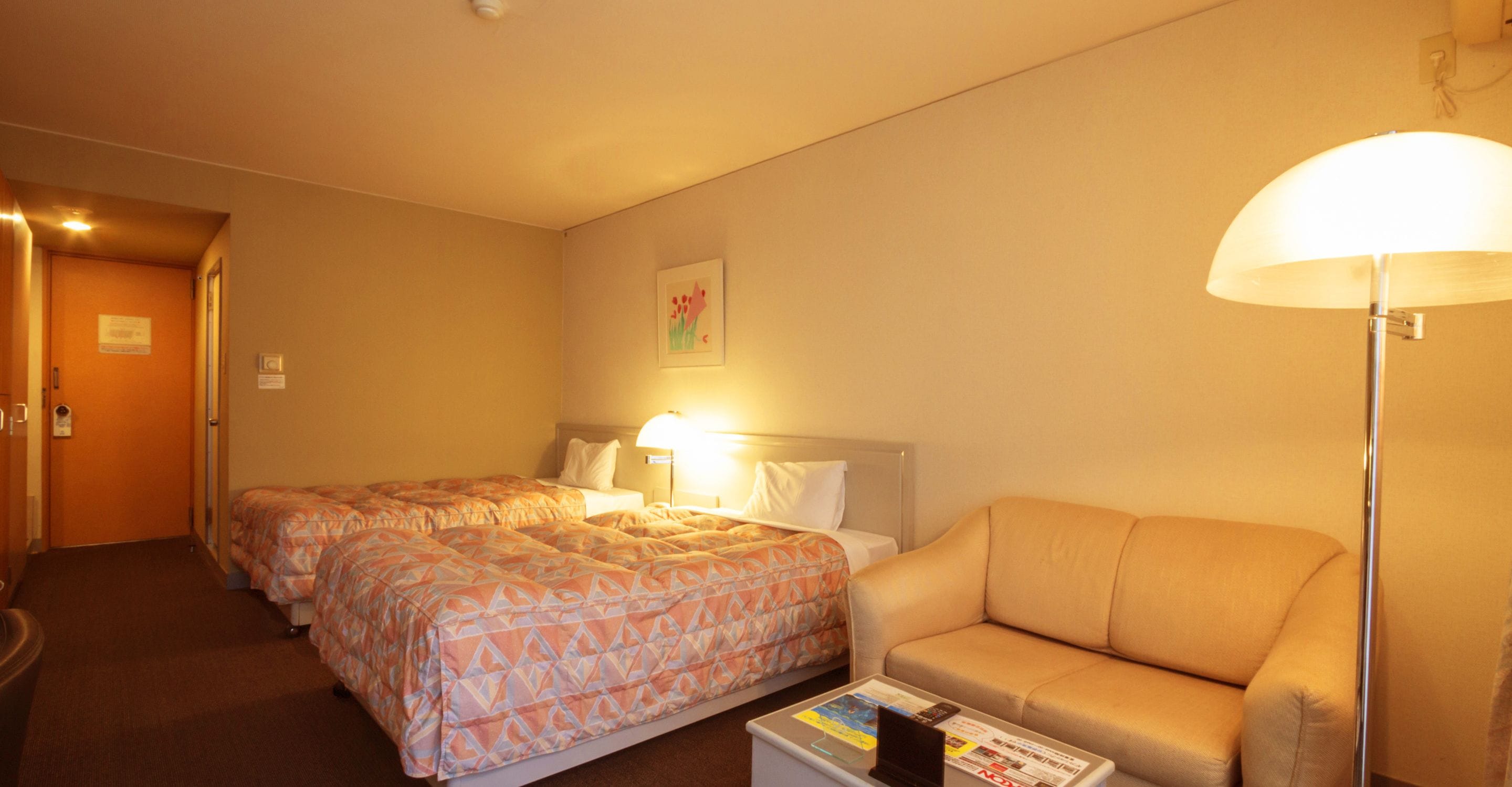 A hotel room with two beds, a sofa, a lamp, and a small table with magazines.