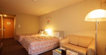 A hotel room with two beds, a sofa, a lamp, and a small table with magazines.