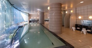 A modern indoor pool area with a glass barrier, tiled flooring, and a row of white stools. - Tsumagoi Resort Sai No Sato (Kakegawa)