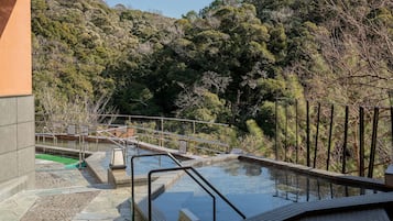 A pool area with a stone deck, metal railings, and a view of a forested hillside.