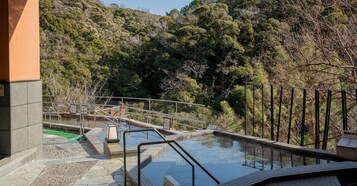 Zona de piscina con terraza de piedra, barandillas de metal y vista a un cerro boscoso.