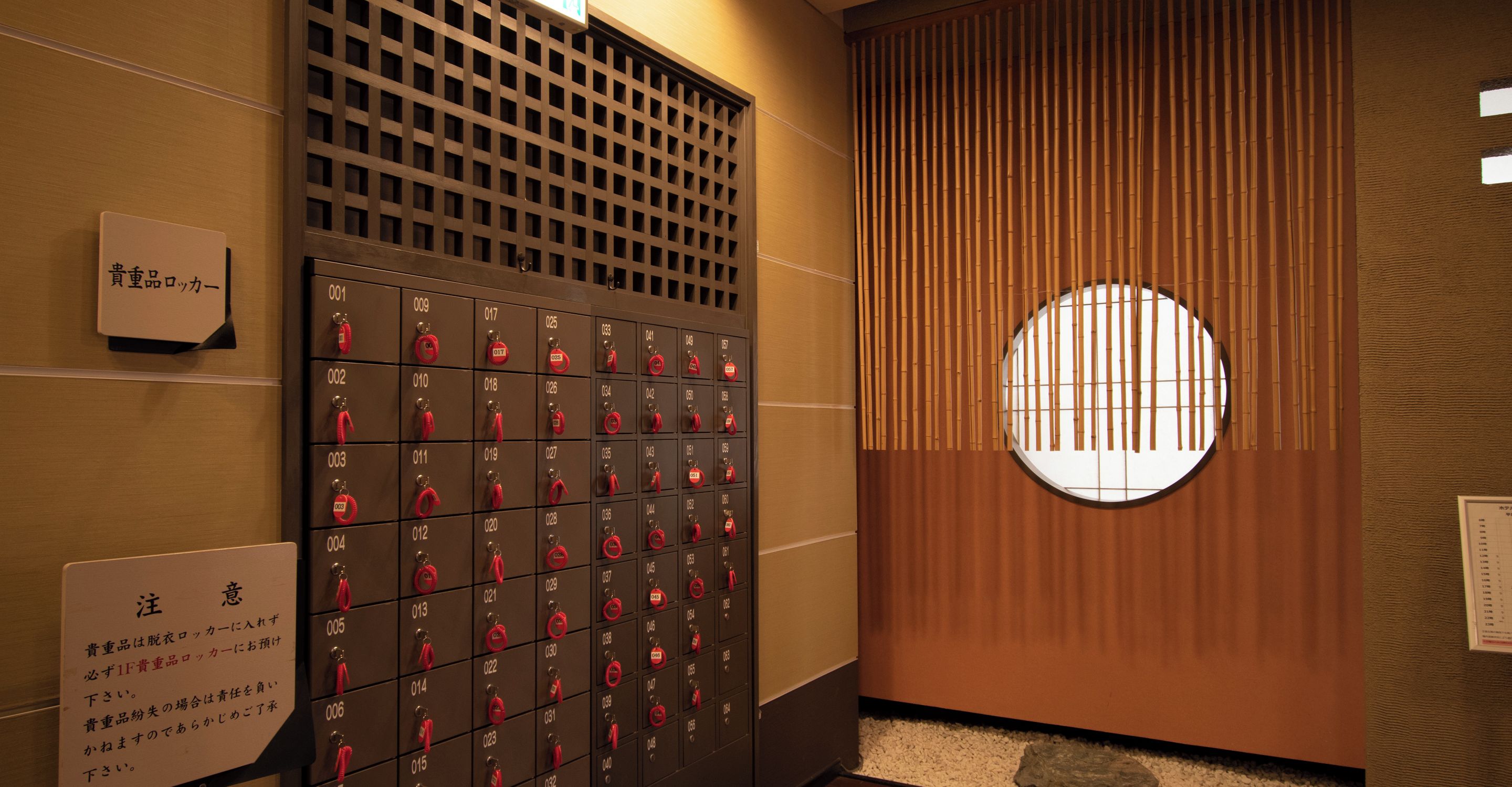 A row of hotel lockers with numbered compartments and red keys.