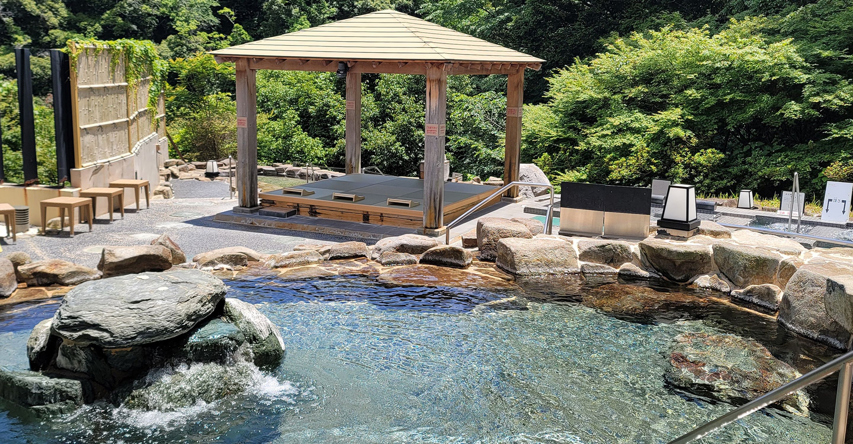 A hot spring area with a wooden gazebo, stone seating, and a small pool.