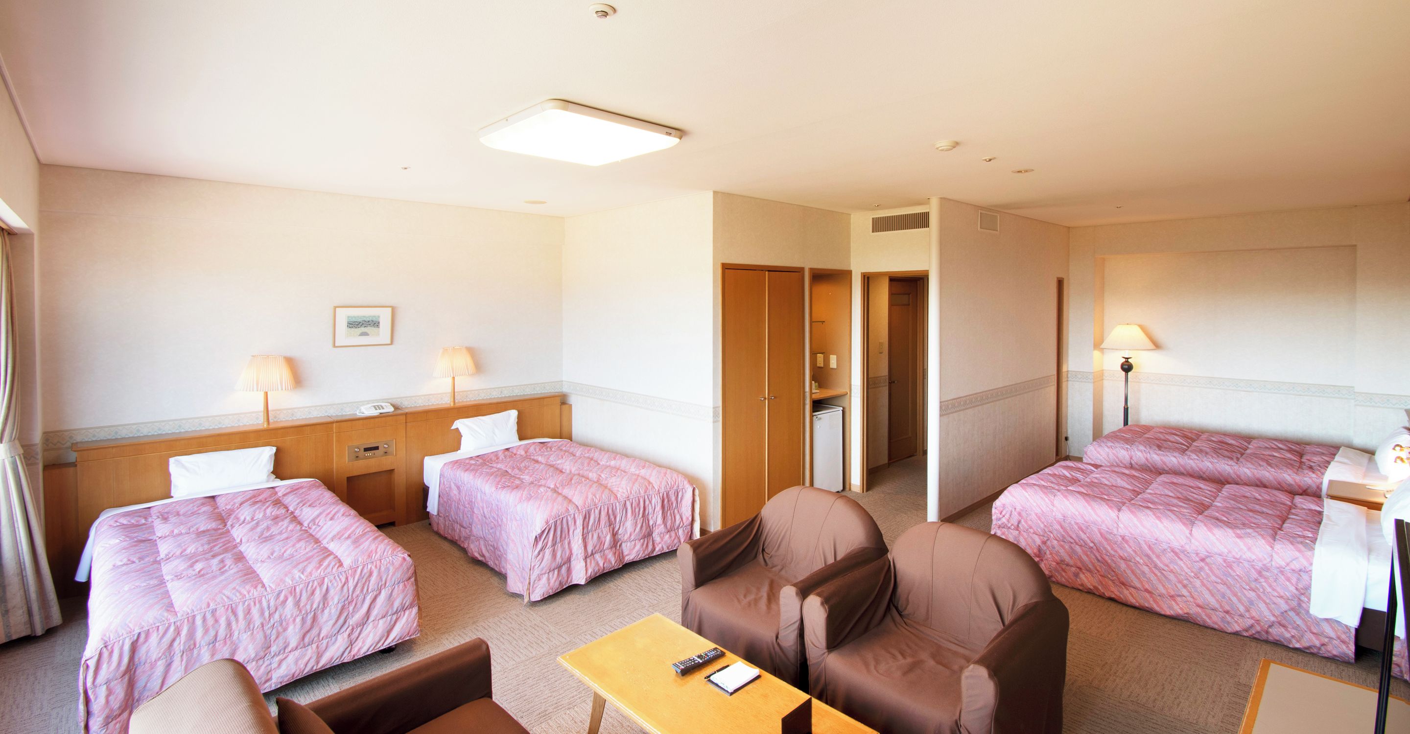 Quarto de hotel com duas camas, uma escrivaninha, uma cadeira, mesa de cabeceira e abajur.