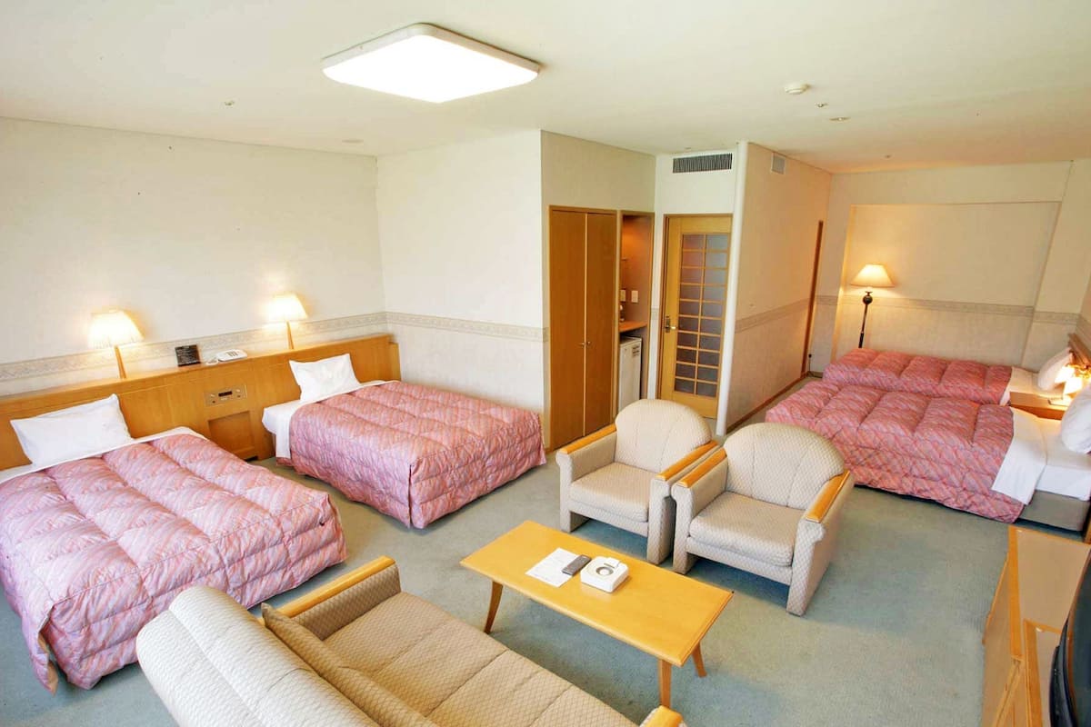 A hotel room with two single beds, a sofa, a chair, a small table, and a wardrobe.