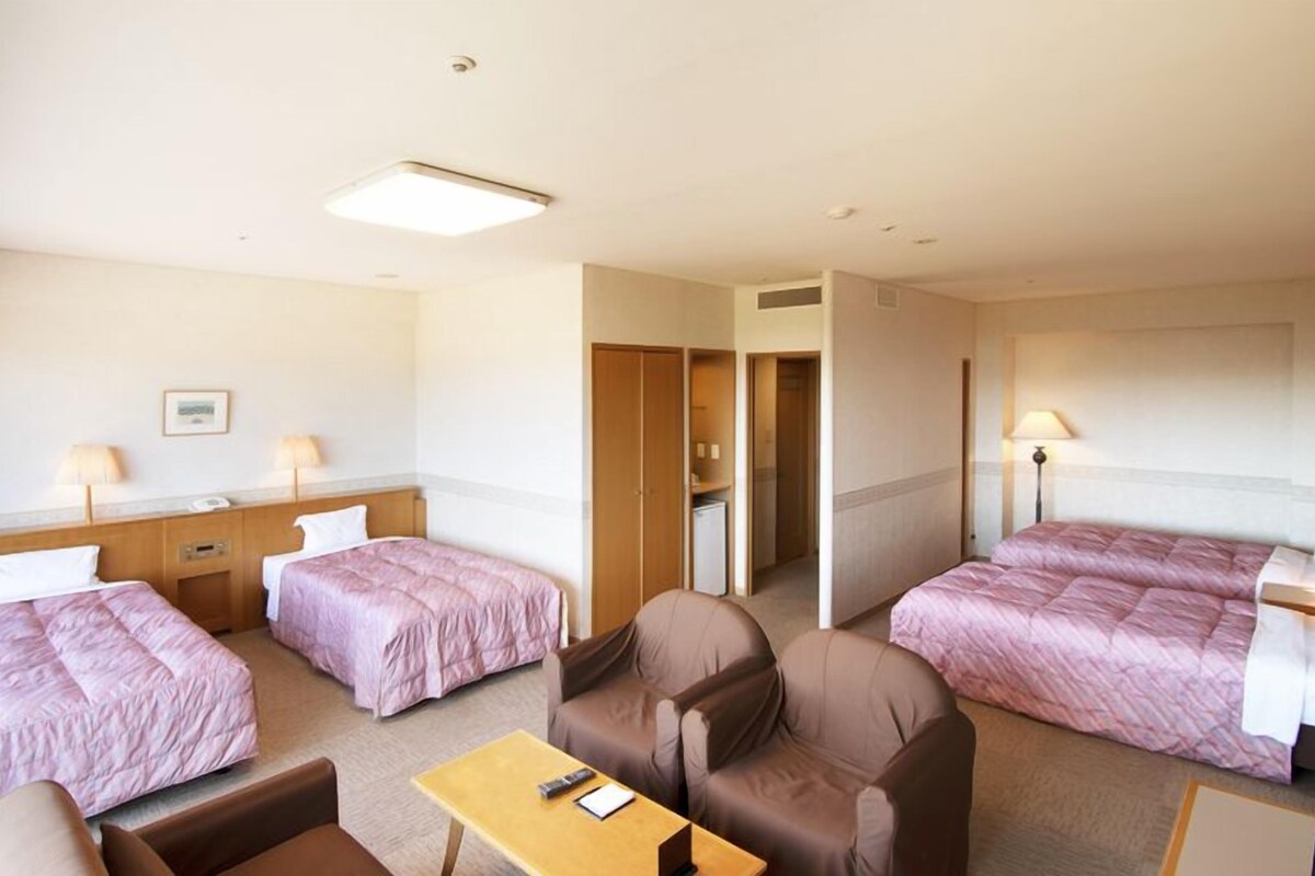A hotel room with two single beds, a sofa, a table, and a desk with a lamp.