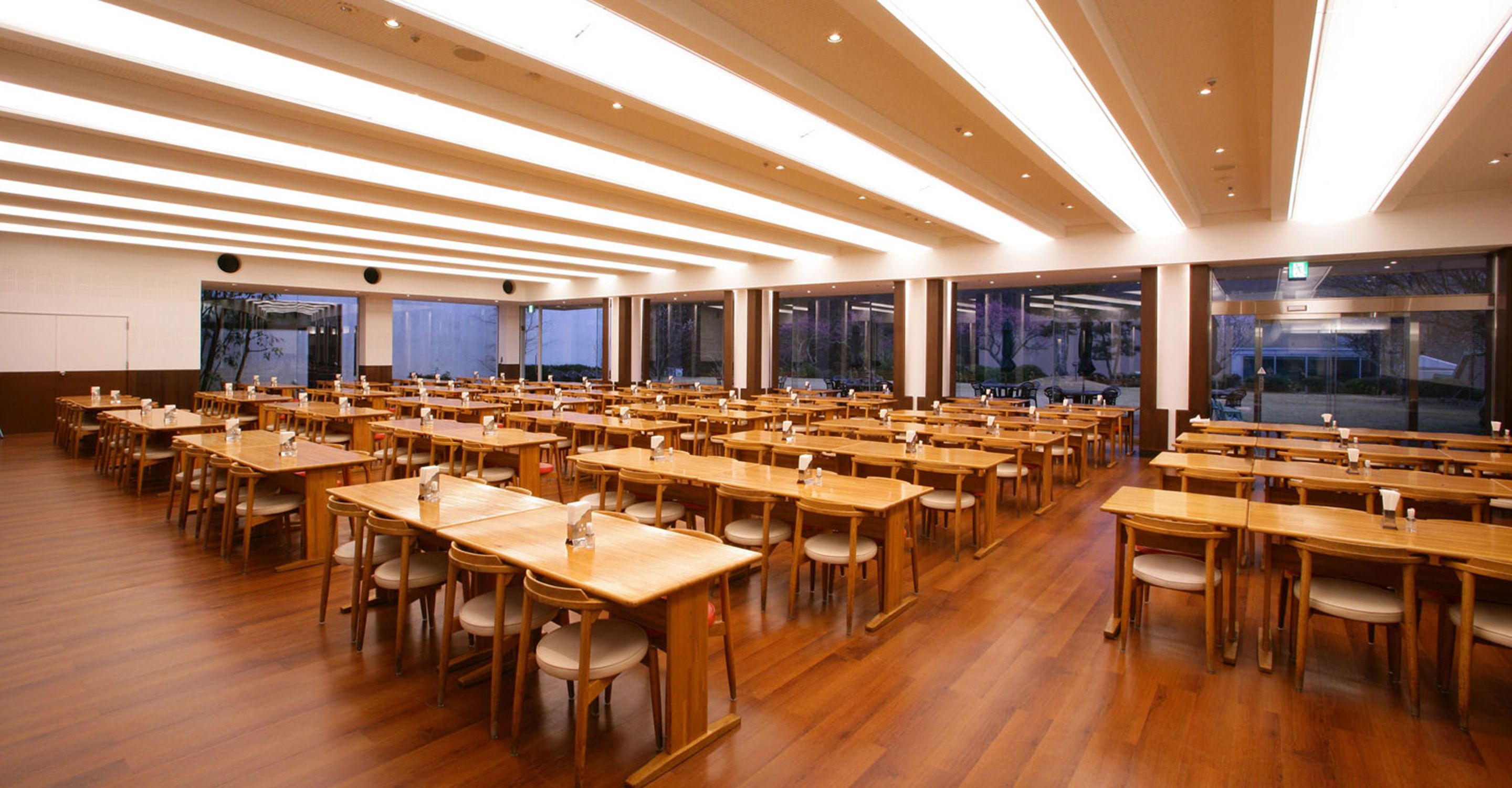 A large, well-lit conference room with numerous tables and chairs, high ceilings, and large windows.