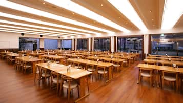 A large, well-lit conference room with numerous tables and chairs, high ceilings, and large windows.