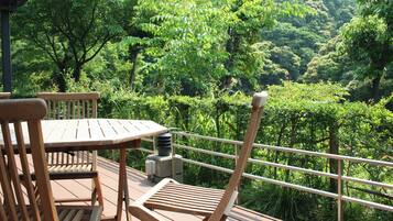 Una terraza de madera con mesa y sillas, con vista a un bosque verde y frondoso.