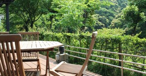 A wooden deck with a table and chairs, overlooking a lush green forest. - Tsumagoi Resort Sai No Sato (Kakegawa)