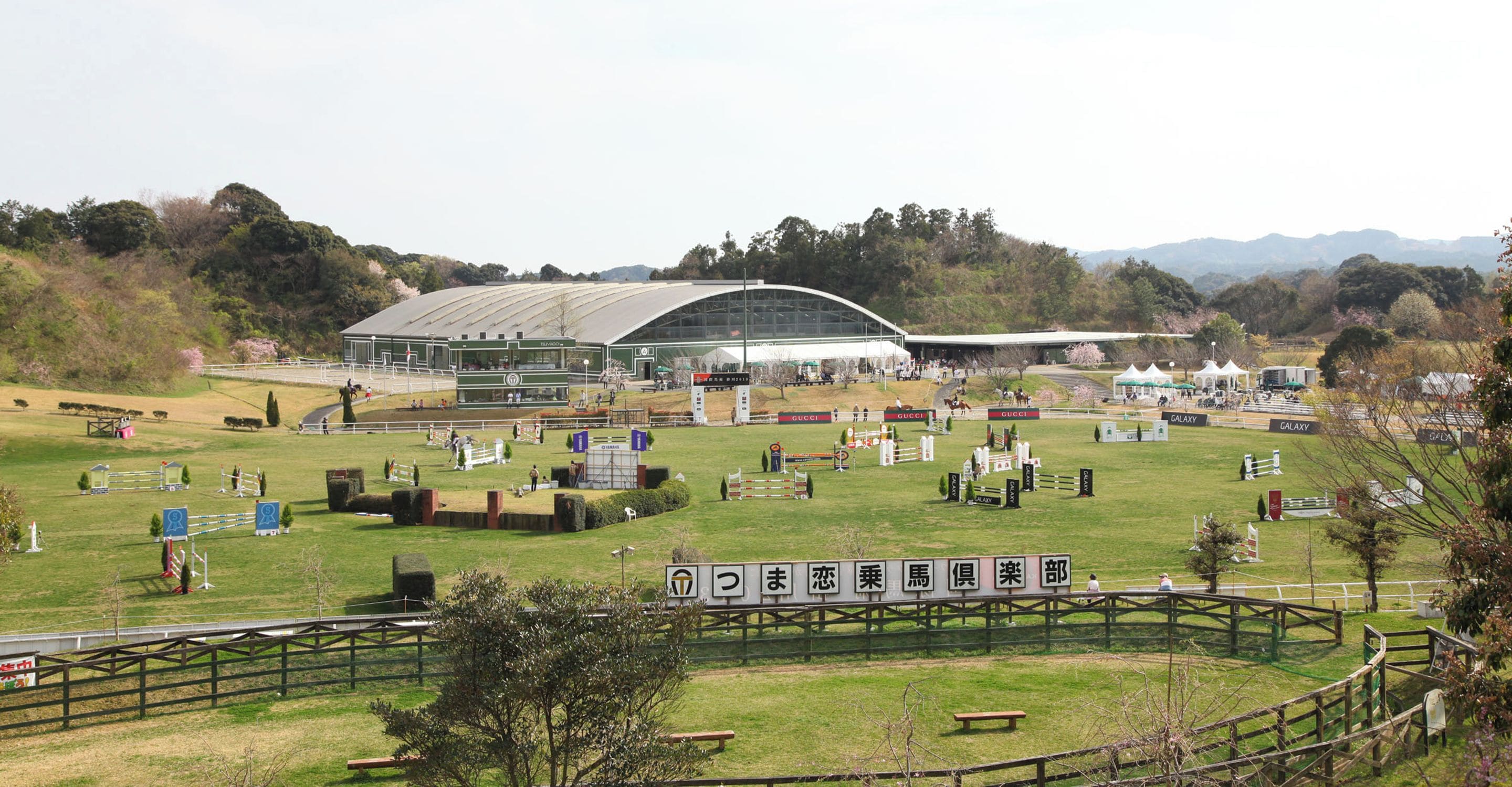 An equestrian event with a large covered arena, multiple jumps, and spectators.