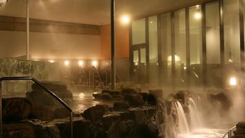 A steam room with hot springs, stone walls, and a wooden floor.
