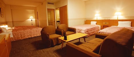 A hotel room with two single beds, a sofa, a small table, and a chair.