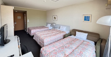 Habitación de hotel con dos camas, un escritorio, un televisor y una puerta que da a otra habitación.