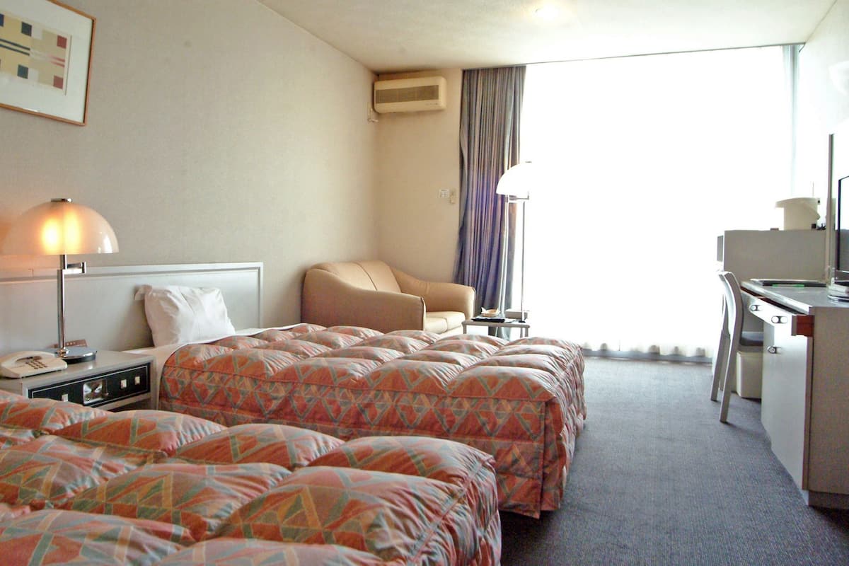 A hotel room with two beds, a desk, a chair, a lamp, and a window with curtains.