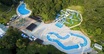 Vista aérea de un parque acuático con múltiples piscinas, toboganes y un amplio espacio abierto con sombrillas.