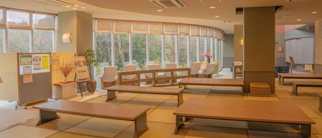Ein modernes Interieur mit Tatami-Matten, Holzbänken und großen Fenstern mit Blick auf Bäume.