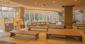 Un interior moderno con esteras de tatami, bancos de madera y grandes ventanales con vistas a árboles.