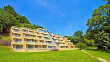A multi-story hotel with a central staircase, surrounded by lush greenery and a clear blue sky.