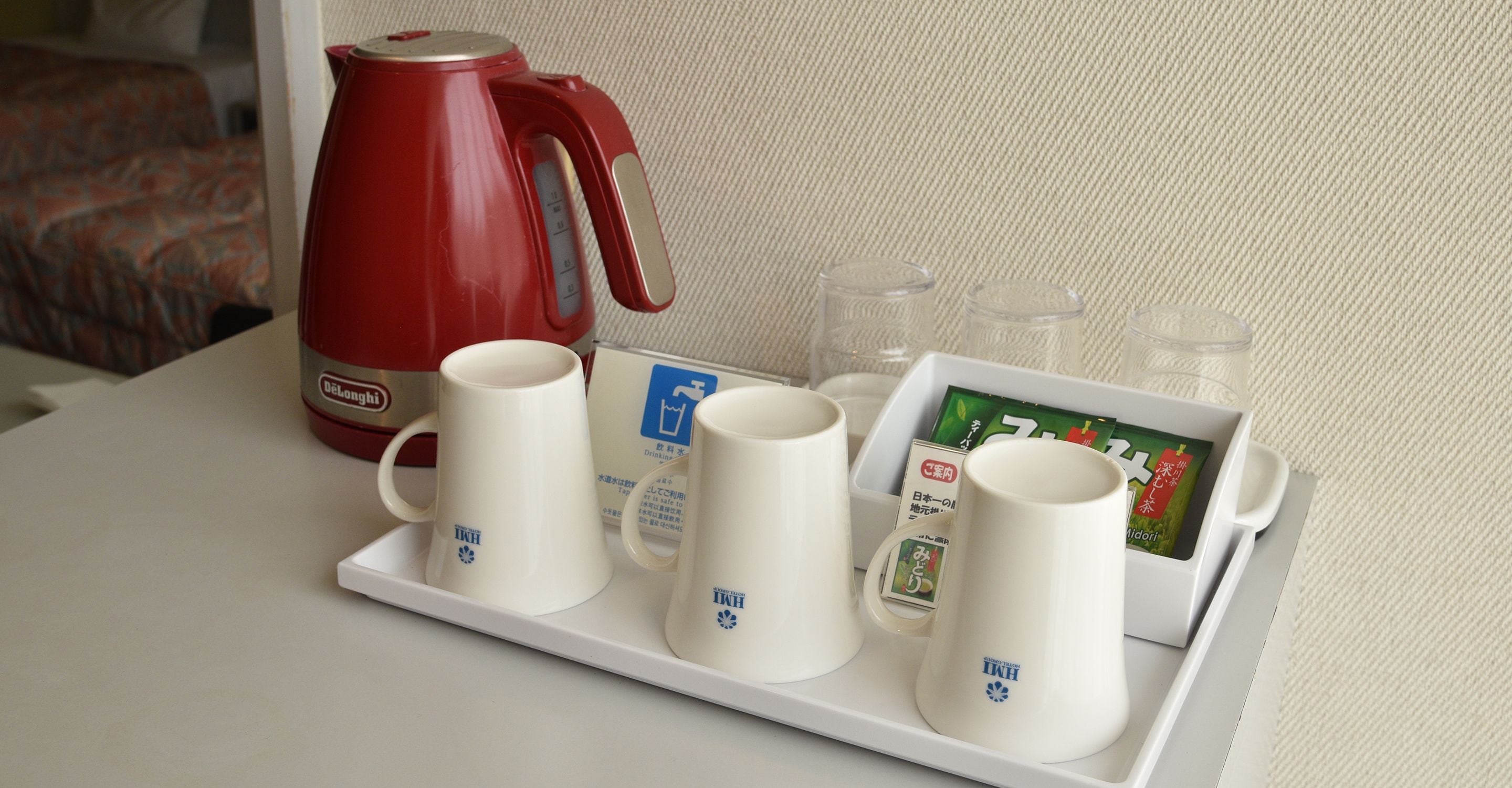 A tray with four white mugs, a red kettle, and a card with Japanese text.