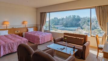A hotel room with two beds, a sofa, a coffee table, a TV, and a view of a building and trees.