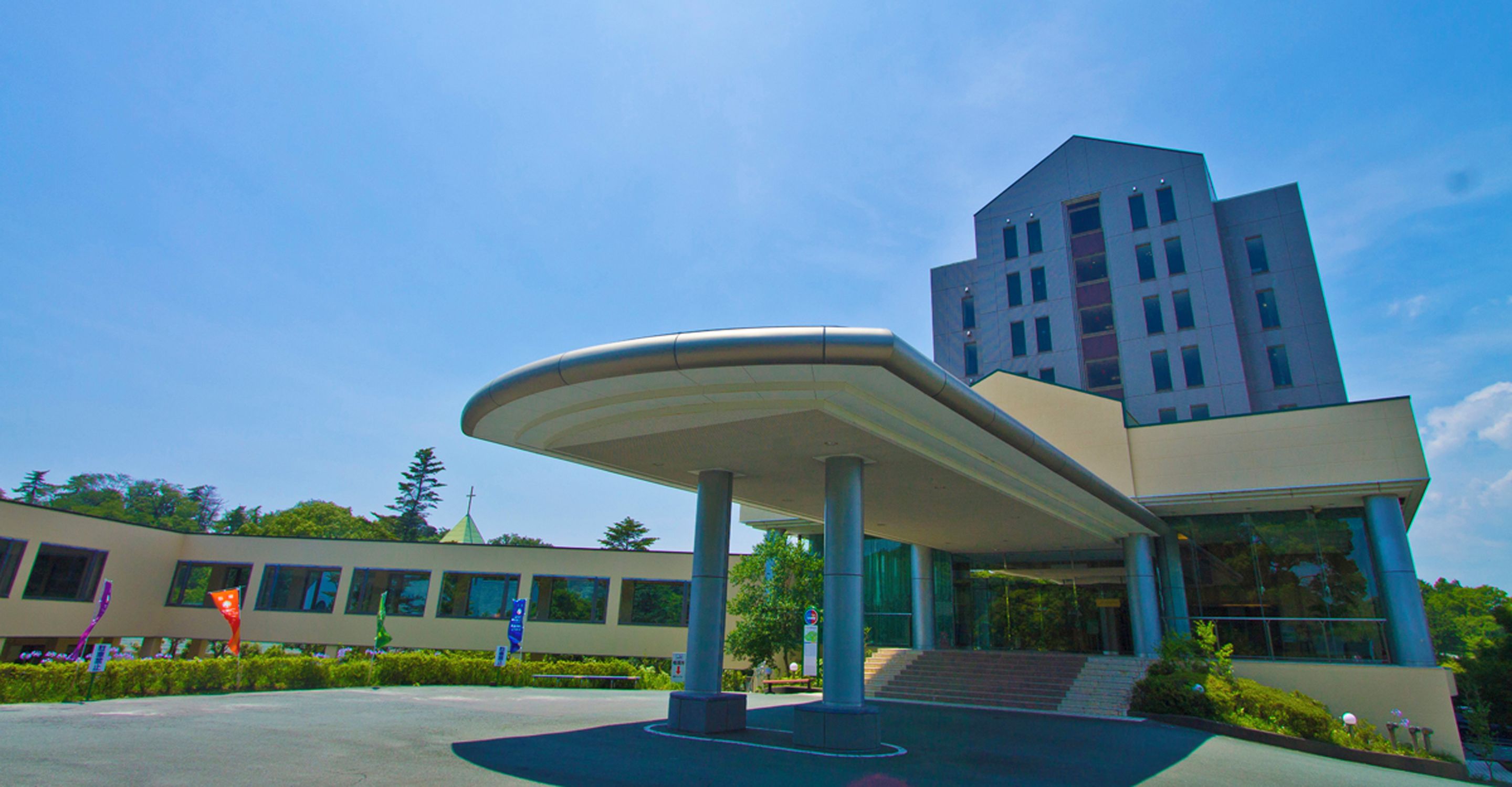 A modern building with a curved roof structure, a staircase leading to the entrance, and a clear blue sky.