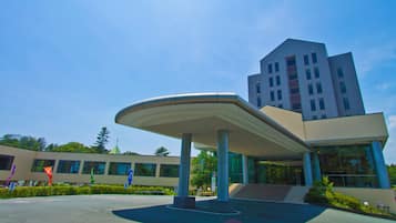 A modern building with a curved roof structure, a staircase leading to the entrance, and a clear blue sky.