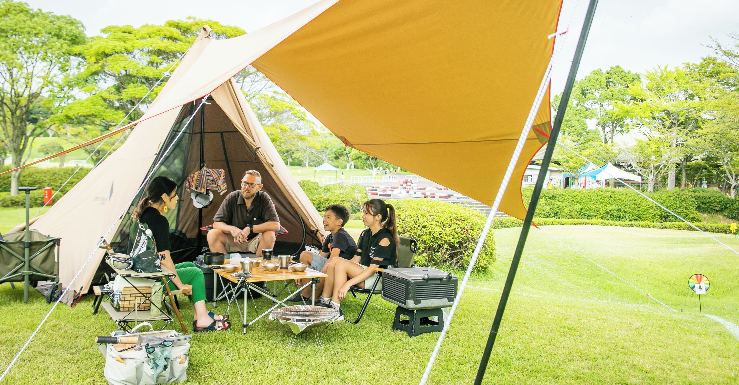 Een groep mensen zit aan een tafel onder een grote tent in een openlucht setting.