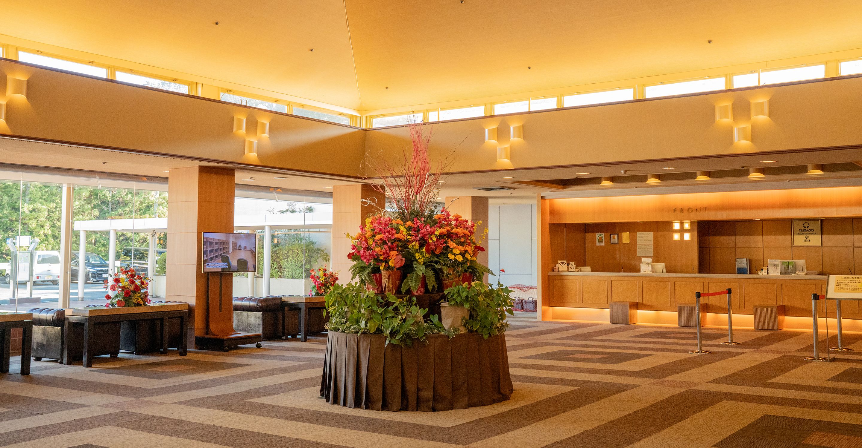 Um hall de hotel com balcão de recepção, área de estar e um grande arranjo floral.