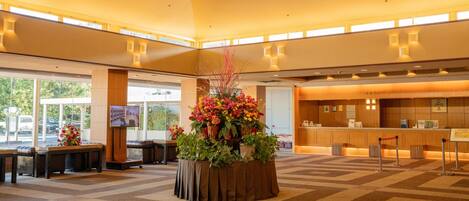 Um hall de hotel com balcão de recepção, área de estar e um grande arranjo floral.